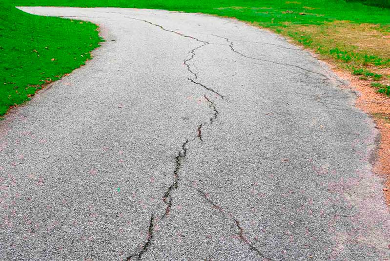 A cracked road stretches into the distance, with lush green grass visible in the background